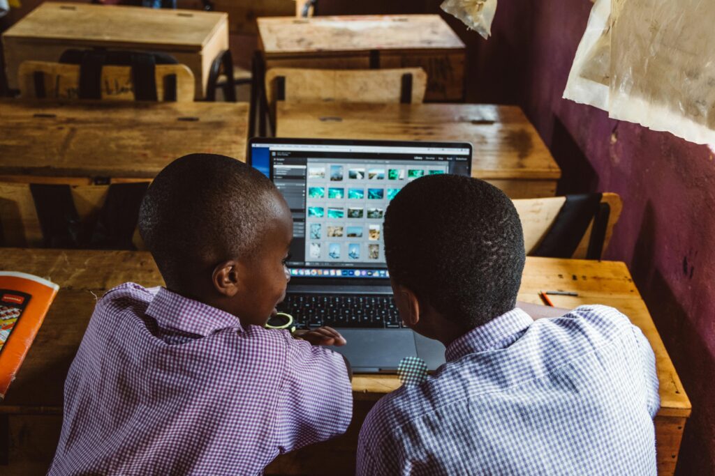 Two boys in school uniforms using a laptop in a classroom, promoting teamwork and technology in education.